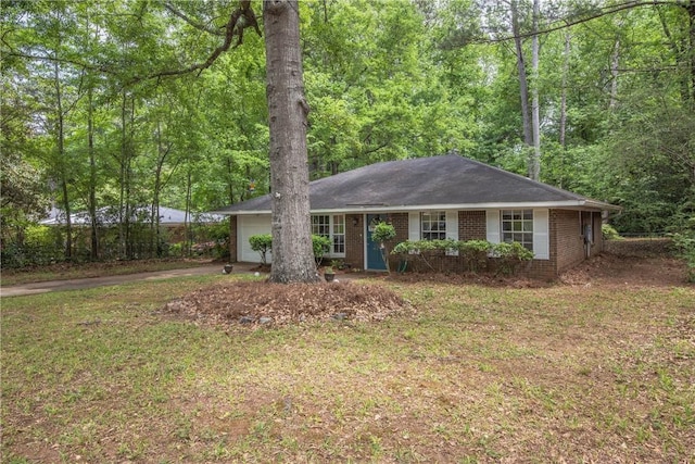 ranch-style home with a garage, a front lawn, brick siding, a view of trees, and driveway