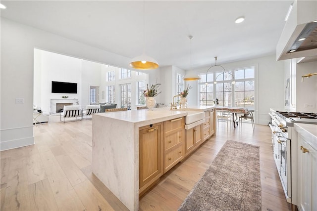 kitchen featuring light wood-style flooring, high end stainless steel range oven, under cabinet range hood, light brown cabinets, and a sink