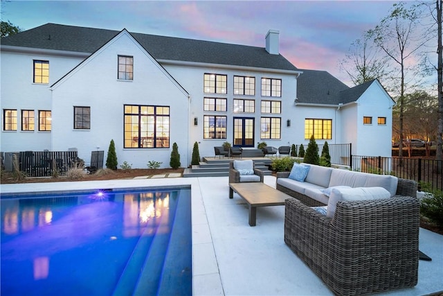back of house at dusk featuring outdoor lounge area, a chimney, fence, french doors, and a fenced in pool
