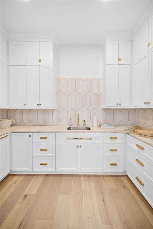 kitchen with a sink, white cabinetry, light countertops, decorative backsplash, and light wood finished floors