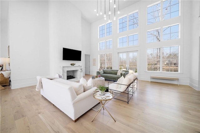 living area featuring baseboards, wood finished floors, french doors, a fireplace, and a chandelier