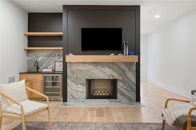 sitting room with beverage cooler, a premium fireplace, wood finished floors, visible vents, and indoor wet bar