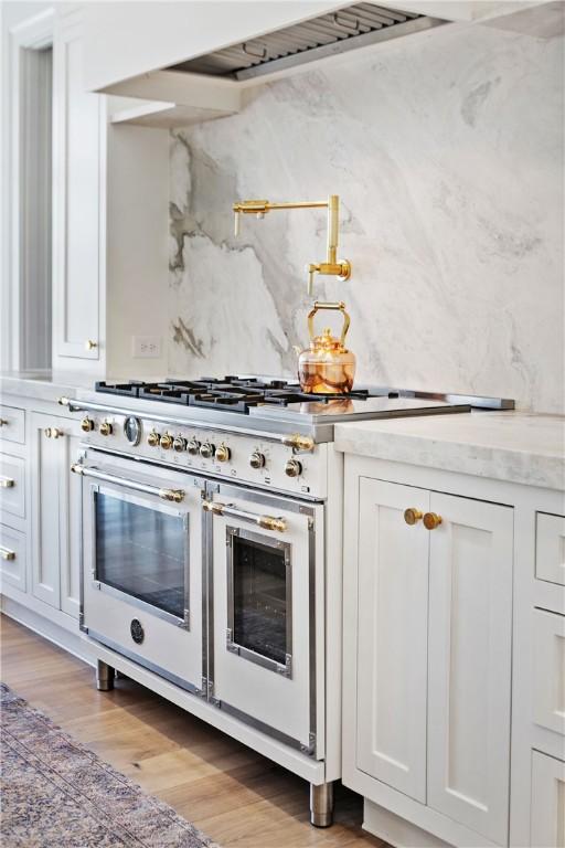 kitchen featuring tasteful backsplash, white cabinets, light stone countertops, light wood-style floors, and double oven range