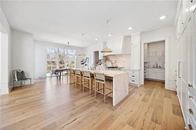 kitchen with light countertops, decorative backsplash, wall chimney range hood, light wood-type flooring, and a kitchen bar