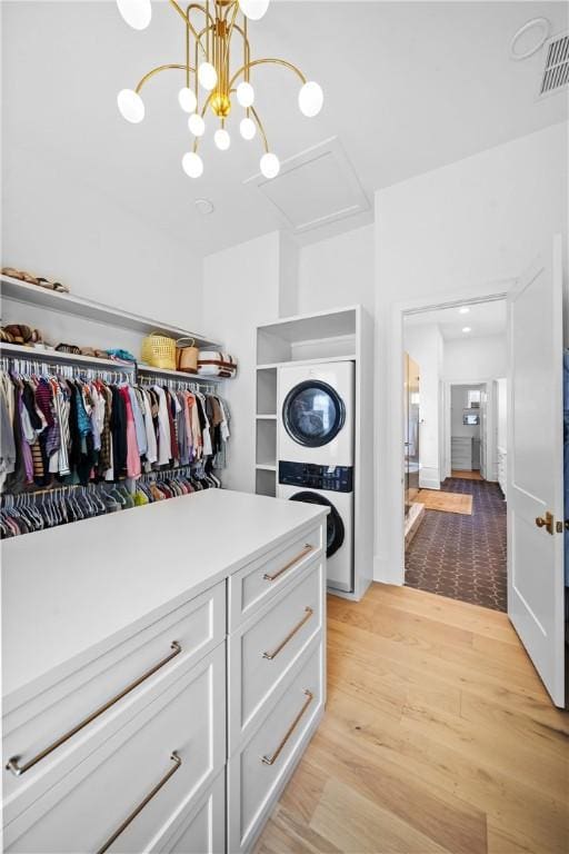 walk in closet featuring light wood-type flooring, stacked washer / drying machine, and visible vents