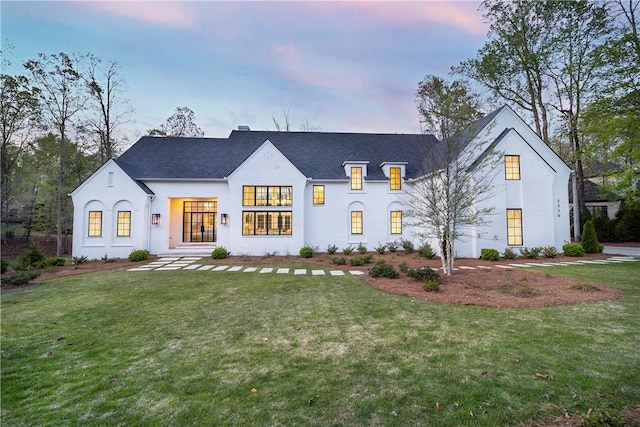modern farmhouse featuring a yard, stucco siding, and a shingled roof