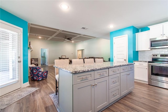 kitchen featuring ceiling fan, tasteful backsplash, wood-type flooring, a breakfast bar area, and stainless steel appliances