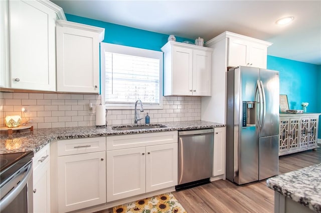 kitchen with stainless steel appliances, backsplash, white cabinets, light stone counters, and sink