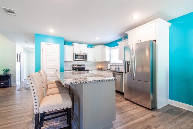 kitchen with light stone countertops, white cabinets, a kitchen island, stainless steel appliances, and a breakfast bar area