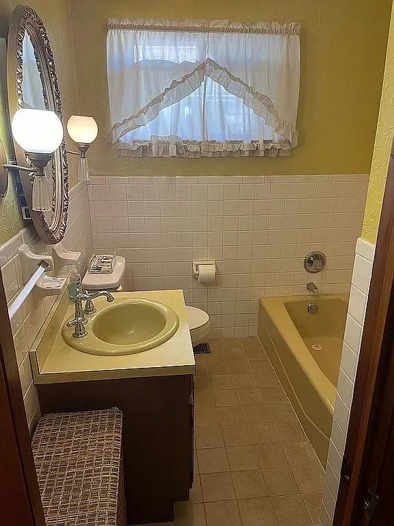 bathroom featuring tile patterned floors, vanity, tile walls, toilet, and a bathing tub