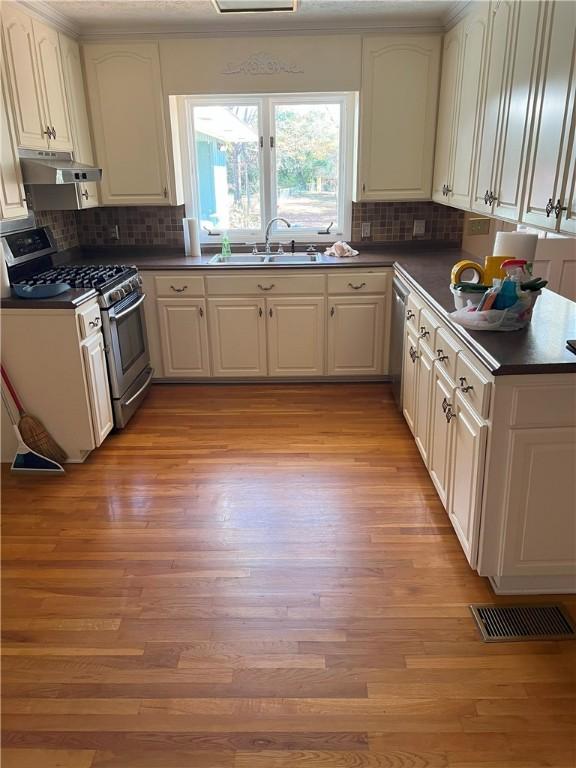 kitchen with appliances with stainless steel finishes, light wood-type flooring, white cabinets, and sink