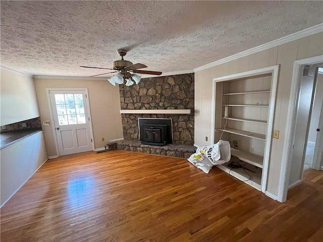 unfurnished living room with ornamental molding, a wood stove, hardwood / wood-style flooring, a textured ceiling, and built in shelves