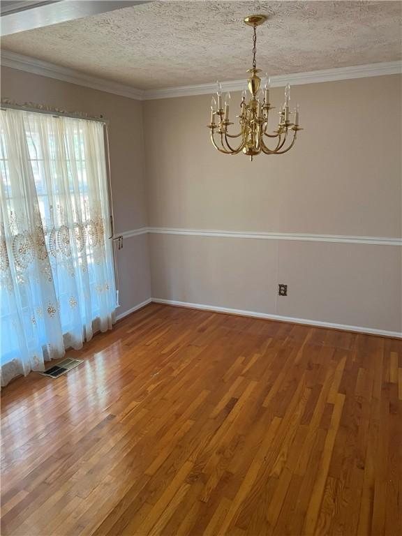 spare room featuring a textured ceiling, ornamental molding, and an inviting chandelier