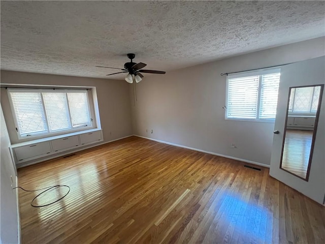 unfurnished room with ceiling fan, light wood-type flooring, and a textured ceiling