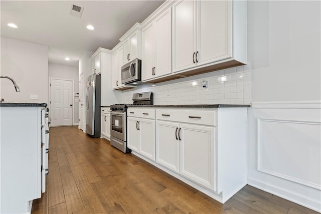 kitchen with wood-type flooring, stainless steel appliances, white cabinetry, and dark stone countertops