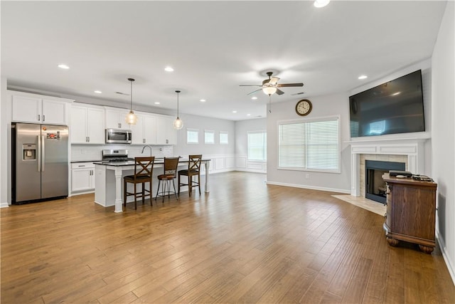 kitchen featuring decorative light fixtures, a kitchen bar, a center island with sink, white cabinets, and appliances with stainless steel finishes