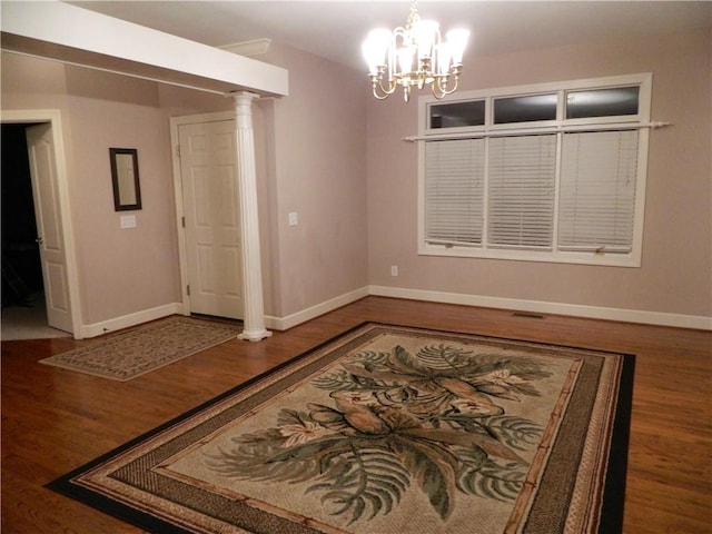 unfurnished room with dark hardwood / wood-style flooring, decorative columns, and a notable chandelier