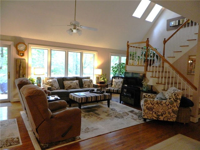 living room featuring ceiling fan, wood-type flooring, high vaulted ceiling, and a skylight