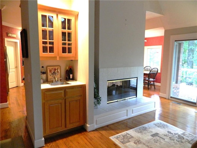 bar with stainless steel fridge, light hardwood / wood-style floors, sink, and a fireplace