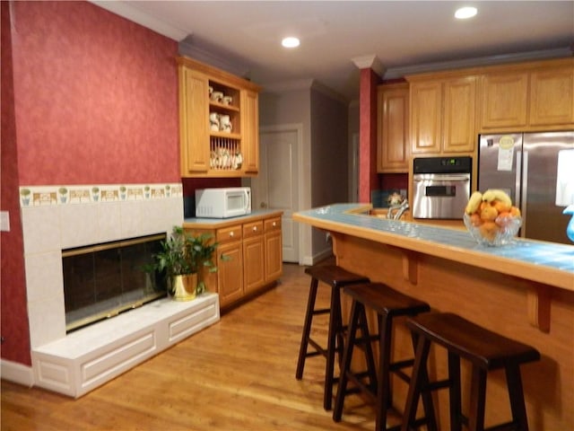 kitchen featuring crown molding, a kitchen bar, stainless steel appliances, and a tile fireplace