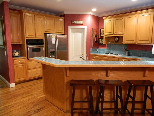 kitchen with tile countertops, a kitchen bar, kitchen peninsula, and appliances with stainless steel finishes