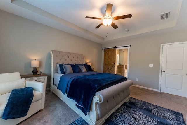 carpeted bedroom featuring a barn door, a ceiling fan, visible vents, baseboards, and a tray ceiling