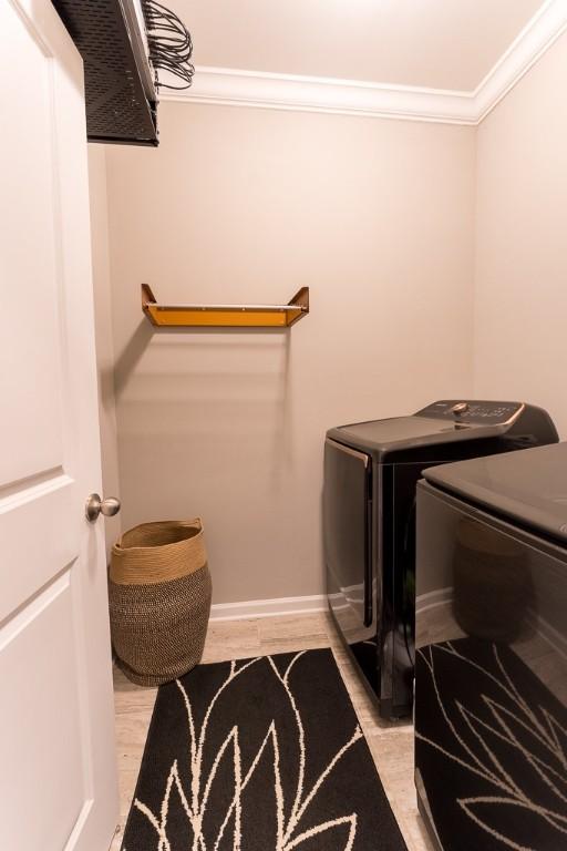 clothes washing area featuring crown molding, washer and clothes dryer, light wood finished floors, laundry area, and baseboards