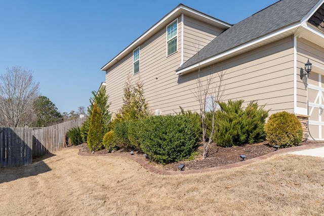 view of side of home with a shingled roof, fence, and an attached garage