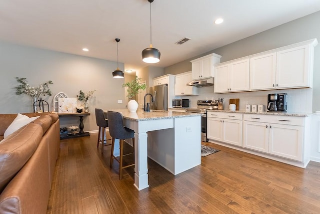 kitchen with dark wood-style floors, stainless steel appliances, visible vents, under cabinet range hood, and a kitchen bar