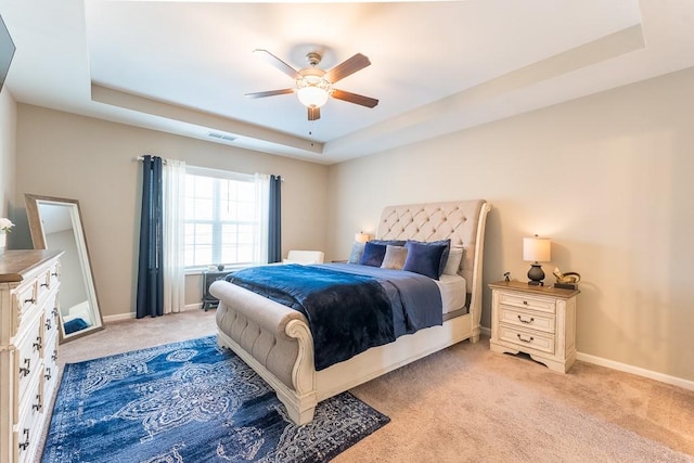 bedroom featuring a raised ceiling, light colored carpet, visible vents, a ceiling fan, and baseboards