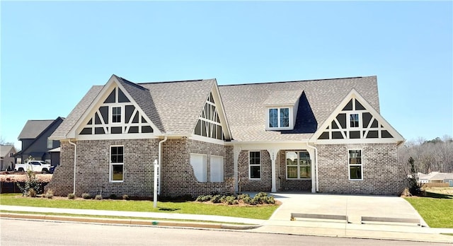 tudor house with brick siding, a front yard, and a shingled roof