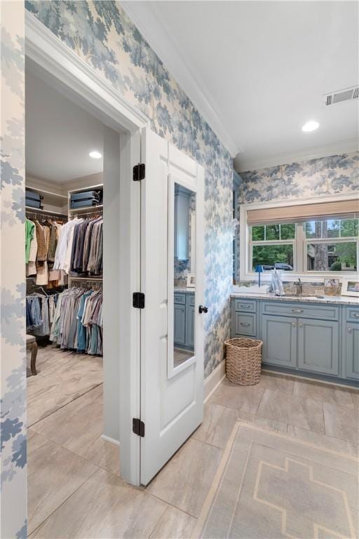 interior space with a walk in closet, vanity, visible vents, and wallpapered walls