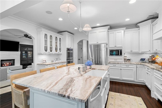 kitchen with appliances with stainless steel finishes, arched walkways, white cabinets, and a ceiling fan