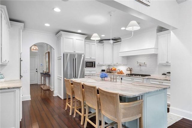 kitchen with arched walkways, dark wood finished floors, tasteful backsplash, appliances with stainless steel finishes, and white cabinetry