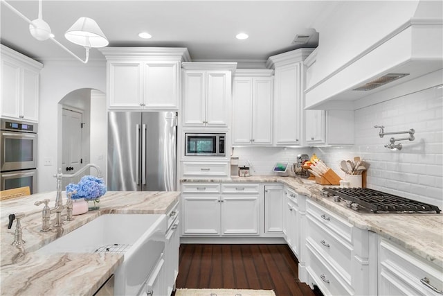 kitchen with arched walkways, custom range hood, decorative backsplash, appliances with stainless steel finishes, and white cabinetry