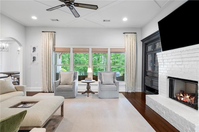 living area with arched walkways, a fireplace, wood finished floors, and visible vents