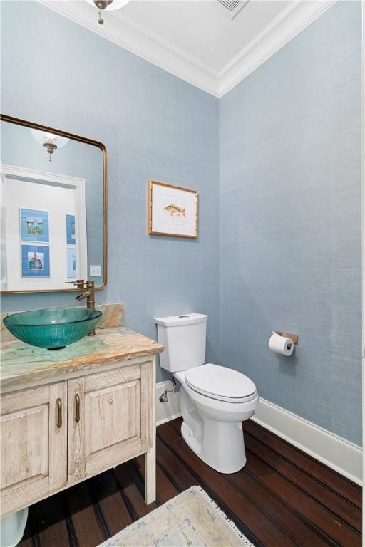 half bathroom with baseboards, toilet, wood finished floors, crown molding, and vanity