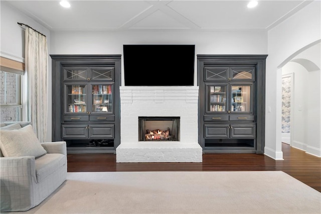 living room featuring arched walkways, recessed lighting, a brick fireplace, wood finished floors, and baseboards