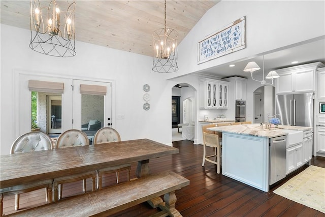 kitchen featuring arched walkways, appliances with stainless steel finishes, dark wood-type flooring, white cabinets, and a kitchen island with sink