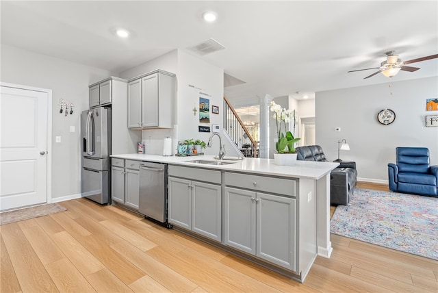 kitchen with a peninsula, appliances with stainless steel finishes, a sink, and gray cabinetry