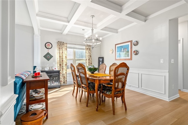 dining area featuring light wood-style flooring, a notable chandelier, a wainscoted wall, coffered ceiling, and beamed ceiling