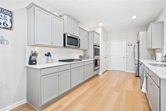 kitchen featuring gray cabinetry, appliances with stainless steel finishes, light wood-style flooring, and decorative backsplash