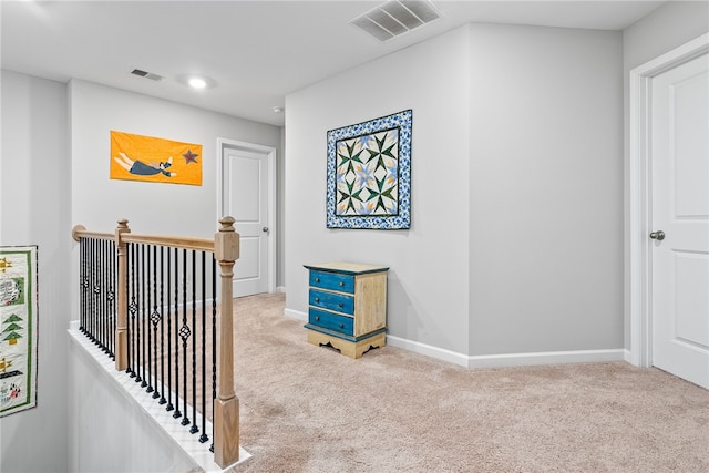 hallway with carpet flooring, visible vents, baseboards, and an upstairs landing