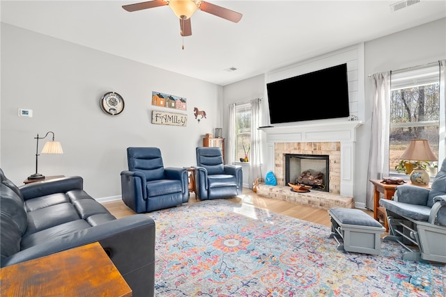 living area with visible vents, baseboards, a ceiling fan, wood finished floors, and a fireplace