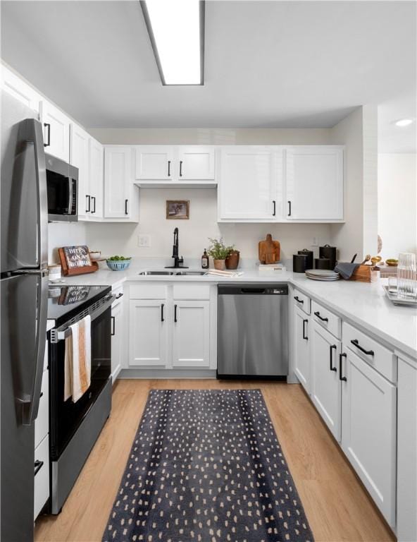 kitchen with white cabinets, stainless steel appliances, light wood-style flooring, and a sink