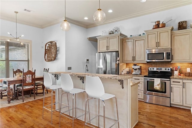 kitchen featuring stainless steel appliances, decorative light fixtures, a kitchen island, and cream cabinetry