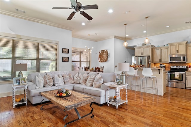 living room with ornamental molding, ceiling fan with notable chandelier, and light wood-type flooring