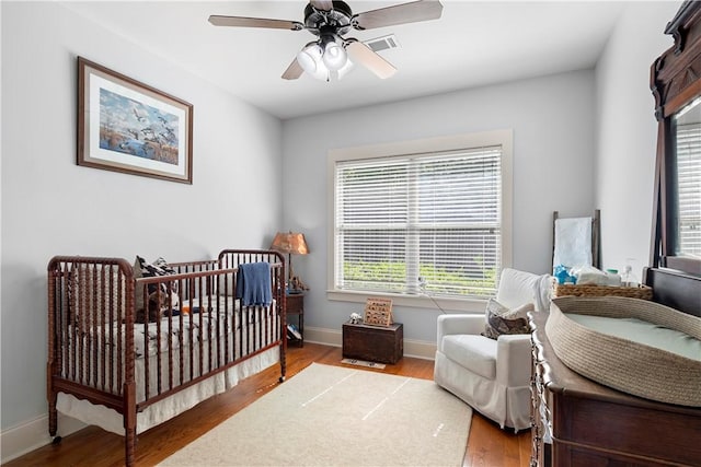 bedroom featuring ceiling fan, light hardwood / wood-style flooring, and a crib