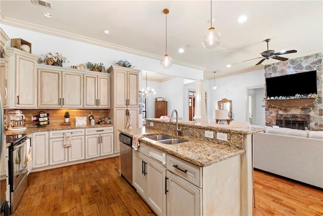 kitchen with pendant lighting, sink, stainless steel appliances, cream cabinets, and a center island with sink