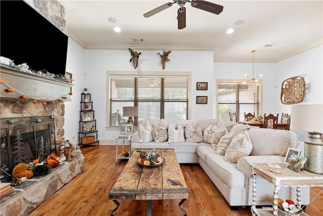 living room with hardwood / wood-style flooring, crown molding, ceiling fan with notable chandelier, and a fireplace